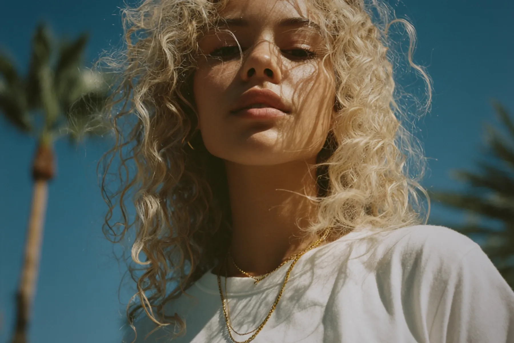 Woman with curly blonde hair looking down toward the camera under a bright blue sky